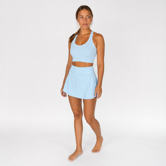 Vrouw draagt de poederblauwe WildForce Azura padelrok met bijpassende racerback crop top, studiofoto vooraanzicht